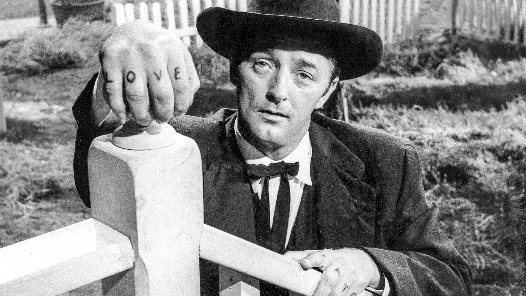 Harry Powell (Robert Mitchum, is looking up from below the porch and holding on to the balustrade. The famous LOVE and HATE tattoos are showing clearly on the back of his fingers.